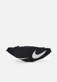 Svart midjeväska i slitstarkt tyg, med en stor vit Nike swoosh-logga och justerbar rem, dragkedjestängning på toppen.
