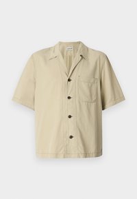 Chemise beige à manches courtes en coton avec un col pointu, fermeture à boutons et poche sur la poitrine gauche. Texture lisse, design simple.