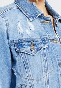 Nött ljusblå denimjacka med silverdetaljer, detaljerad sömnad och klassisk krage med fickor på framsidan.