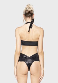 Set bikini nero composto da un top bandeau con nodo al collo e un pantaloncino a vita alta con design incrociato, realizzato in materiale lucido.