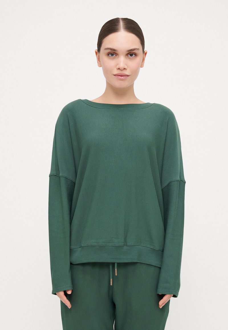 Blusa verde de mangas longas com um decote amplo e costuras de ombro caídas. Feita de tecido macio, apresenta um corte descontraído e um acabamento canelado.