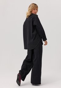 Czarny dżinsowy zestaw z oversize'ową koszulą i spodniami, z zakrzywionym dołem, zapinanymi mankietami, szczegółowym przeszyciem i luźnym krojem. Szpilki w burgundowym kolorze jako akcent.