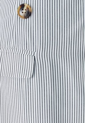 Pruhovaná látka v bílé a černé barvě, s jednou náprsní kapsou a kulatým, světle hnědým knoflíkem se dvěma dírkami.