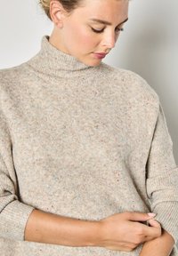 Maglione beige lavorato a maglia con colletto alto, caratterizzato da macchie colorate in tutto il capo e polsini a coste. Texture morbida e vestibilità rilassata.