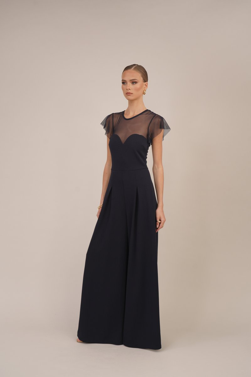 Mørkeblå jumpsuit med en tettsittende bodice, gjennomsiktige flomraggsangermanskjorter og en design med vide bukser. Har en hjerteformet utringning og myk tekstur.