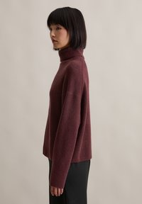 Bordowy sweter z golfem o luźnym kroju, wykonany z miękkiego materiału. Posiada długie rękawy oraz prążkowane wykończenia przy kołnierzu i u dołu.