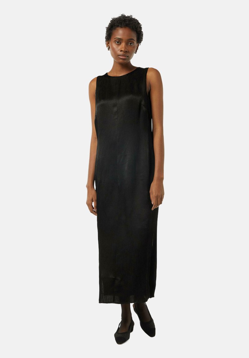 Czarna bezrękawnikowa sukienka o gładkiej fakturze, długości do ziemi, z okrągłym dekoltem, noszona z czarnymi szpilkami.