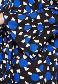 Tessuto nero con grandi pois astratti blu e bianchi, dotato di una manica svasata e dettaglio arricciato al polsino per un tocco di texture in più.