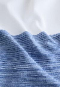 Bomullstyg med en texturerad övergång från ljusblått till mörkblått, uppdelad av en jämn vit sektion. Synliga fina revärsdetaljer.