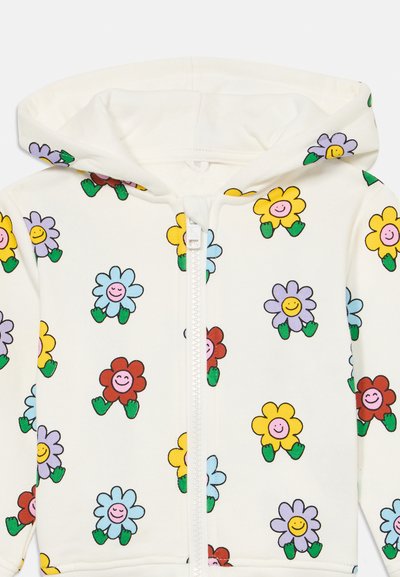 Hettegenser med zip i krem, med fargerike blomster mønstre med smilende ansikter. Laget av myk stoff, ideell for komfort.
