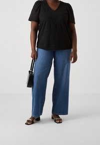 Top de ganchillo negro con mangas cortas abullonadas, escote en V; combinado con pantalones vaqueros de mezclilla azul de pierna ancha. Lleva un pequeño bolso negro. Sandalias negras tipo slide.