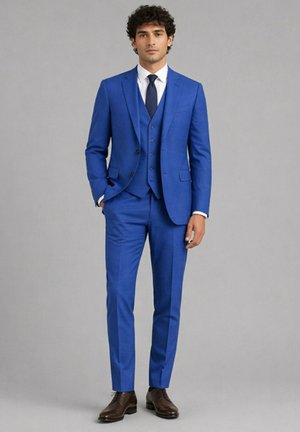 Homme debout portant un costume trois pièces bleu vif, chemise blanche, cravate bleu marine et chaussures marron sur un fond gris uni.