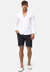 Hvid linned skjorte, navy shorts med opsmøg og hvide slip-on sko. Skjorten har en knap-op design og en klassisk krave.