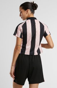 Roza in črna športna kombinacija, ki vključuje krojeno polo majico z navpičnimi črtami in teksturiranim vzorcem, ki je v paru s črnimi kratkimi hlačami.