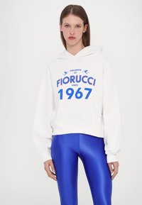Balta sutrumpinta gobtuvė su mėlynu grafiniu tekstu "DREAMING OF FIORUCCI SINCE 1967" ir mėlynomis tamprėmis. Minkšta medžiaga, laisvas siluetas, kišenė kengūrai.