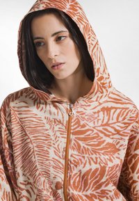 Kapuzensweatjacke mit Reißverschluss aus weichem Stoff, mit einem orange-beigen Blattmuster, einem silbernen Reißverschluss und einer Kängurutasche.
