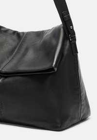 Bolso de hombro de cuero negro con un diseño distendido, cierre de solapa plana, correa ajustable y textura suave. Branding sutil en el lado.