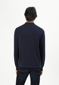 Marineblaues Langarm-Polohemd mit einem gerippten Kragen, das eine glatte Textur und einen geraden Saum aufweist, kombiniert mit dunklen Jeans.