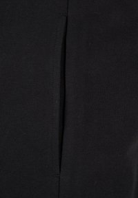 Tela negra con una abertura vertical. El material tiene una textura suave, con un acabado liso y un leve estiramiento. Detalle de costura visible.