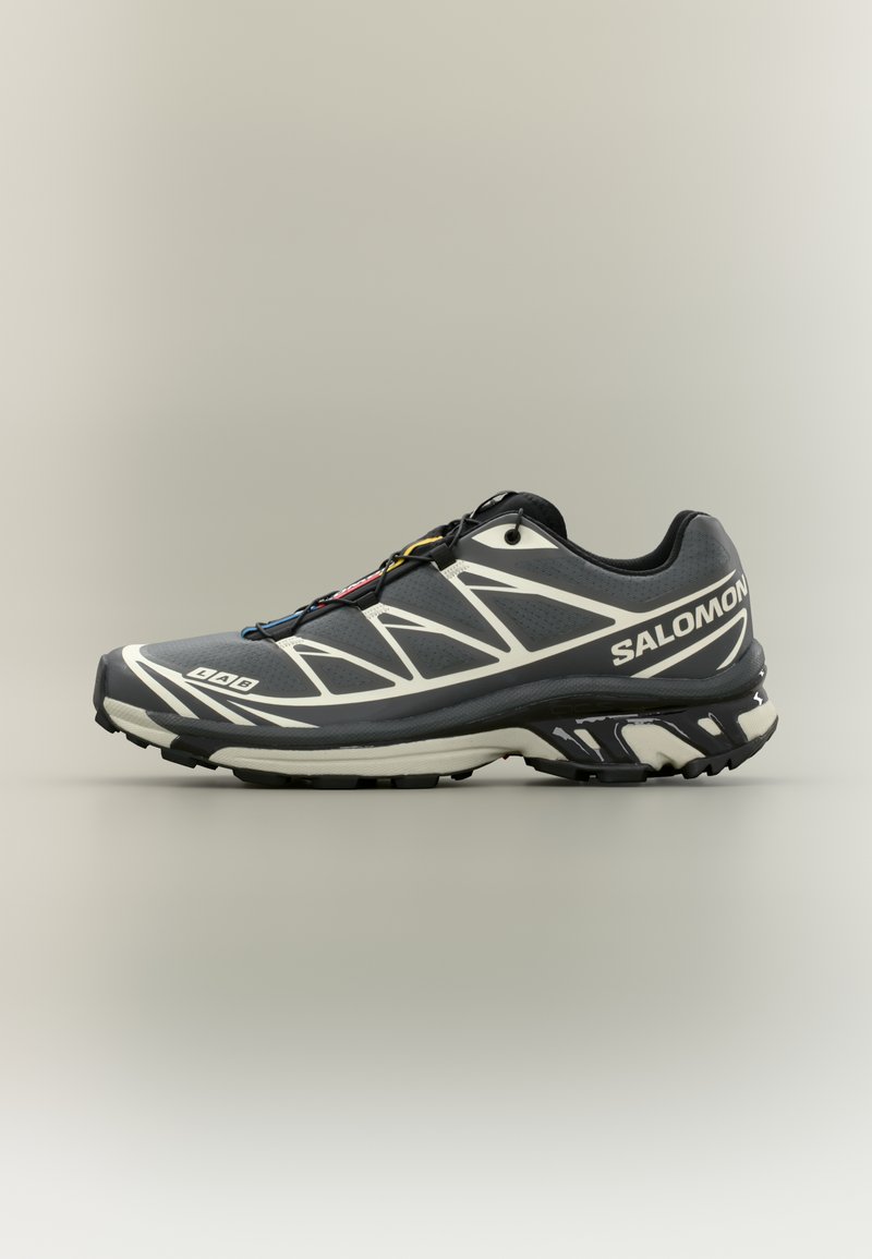 Fekete és szürke futócipő texturált felsőrésszel, fehér díszítésekkel, egyedi talp kialakítással és biztos fűzőrendszerrel.