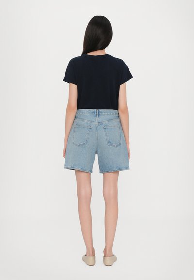 Μπλε τζιν σορτς με άνετη εφαρμογή, ψηλή μέση και τέσσερις τσέπες, συνδυασμένα με ένα μαύρο κοντομάνικο τοπ.