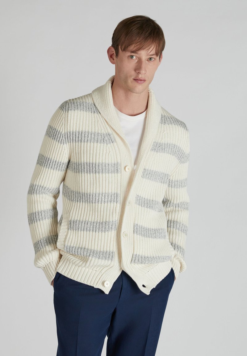Cárdigan a rayas blancas y grises con cuello de chal, textura acanalada, cierre de botones y bolsillos laterales, llevado sobre una camiseta blanca.