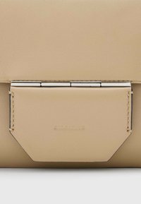 Borsa a tracolla in pelle beige con finitura texture, dotata di una chiusura metallica e dettagli angolari. Branding sottile vicino alla parte inferiore.