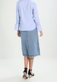 Camicia azzurra con maniche a campana, abbinata a una gonna di denim a lunghezza media con orlo grezzo; scarpe con tacco nere con dettagli a pois.