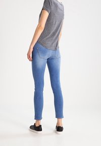 Blue skinny jeans with a smooth texture, five-pocket design, and a slight fade. Paired with a short-sleeve gray shirt and black sneakers.