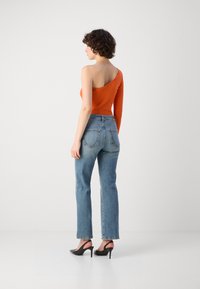 Top arancione a manica unica, slim fit; jeans a vita alta blu, lavaggio chiaro; décolleté neri a punta con cinturino; trame lisce ovunque.