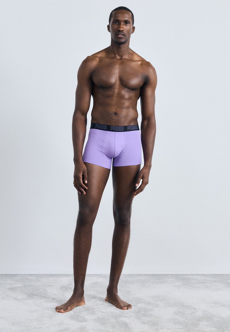 Herre lilla boxershorts med svart merke-elastikk, tilpasset design, glatt stoff og midt på låret lengde. Modell står på en lys overflate.