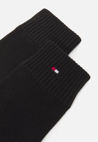 Mustad mustriga sokid, millel on ribadest ääristatud varbad ja väike ikooniline logo punaste, valgete ja siniste aktsentidega ülemises servas.