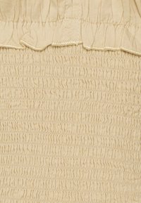 Béžová látka s smockovanou texturou, s úzkými horizontálními nariaseními a volánovým okrajem nahoře. Hladký a jemný vzhled.