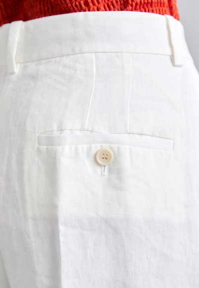 Λευκά λινά παντελόνια διαθέτουν πίσω τσέπη με κλείσιμο από ένα κουμπί, λεία υφή και προσαρμοσμένη εφαρμογή. Παρόντα είναι στοιχεία μινιμαλιστικού σχεδιασμού.