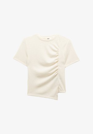Camiseta de manga corta color crema con un tejido texturizado. Presenta fruncidos en los laterales y un dobladillo asimétrico para un detalle de diseño único.