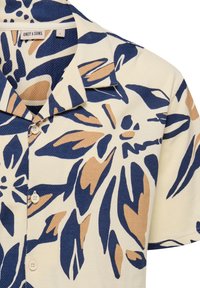 Camisa de manga corta en crema con un estampado floral azul y marrón, tejido texturizado y cuello con botones. Presenta tres botones en el frente.