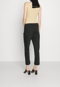 Černé džíny z denimu s volnějším střihem, středním pasem a dvěma zadními kapsami. Spárováno s béžovým bezrukávovým topem a černými botami na blockovém podpatku.