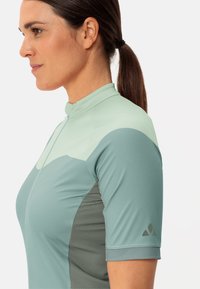Maillot de cyclisme à manches courtes en vert clair et turquoise. Fait d'un tissu lisse et extensible avec un col zippé et un panneau latéral texturé.