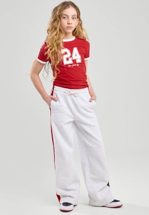 Camiseta roja de manga corta con acentos blancos y una gran impresión del "24"; combinada con pantalones de chándal grises con franjas rojas a los lados y un cordón.