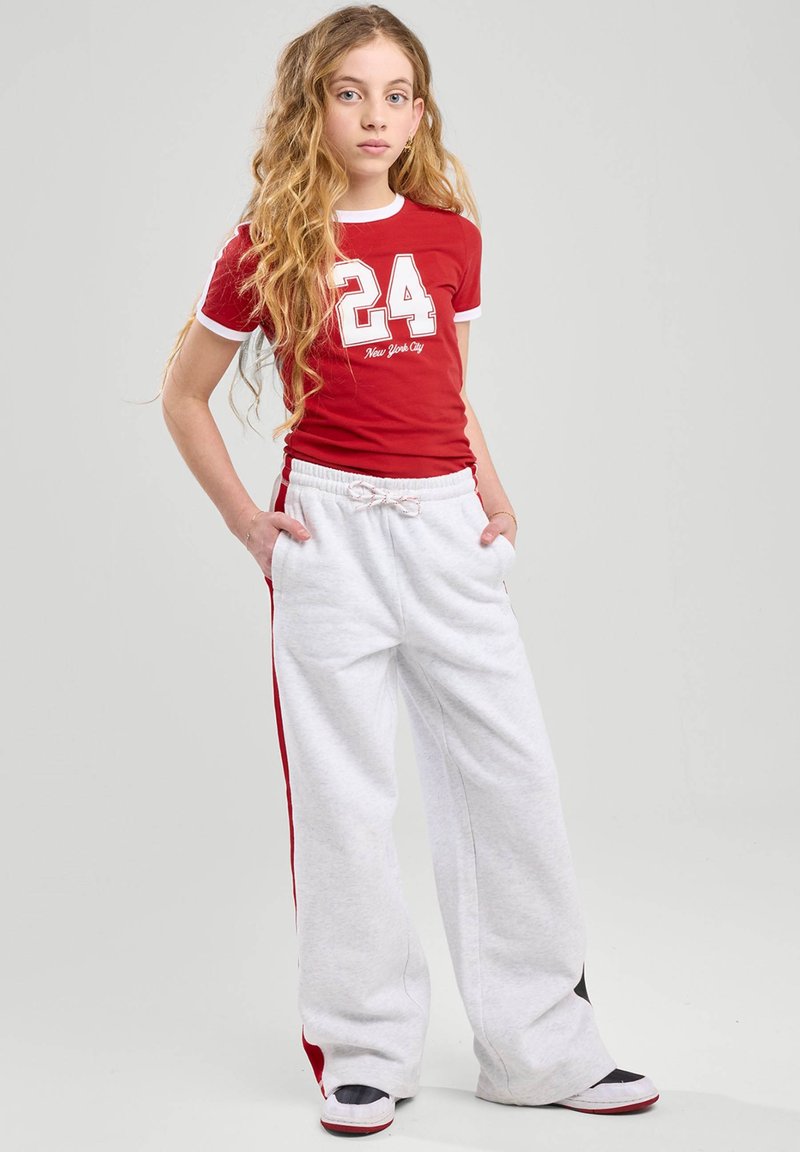 Camiseta roja de manga corta con acentos blancos y una gran impresión del "24"; combinada con pantalones de chándal grises con franjas rojas a los lados y un cordón.