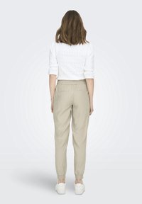 Witte textuur blouse en lichtbeige taps toelopende broek met een elastische tailleband, voorzien van zijzakken en geribde enkels. Witte sneakers.