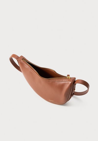 Bolsa transversal em forma de meia-lua de couro castanho com fecho dourado e alça ajustável sobre fundo branco.