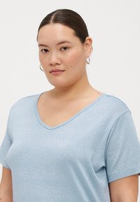 Camiseta V azul clara feita de um tecido texturizado e brilhante; mangas curtas; corte descontraído; brilho subtil; design minimalista.