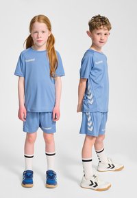 Ljusblå träningsset med korta ärmar och shorts. Har logotyp och sidovinkelmönster. Barnen bär vita strumpor och sportskor.