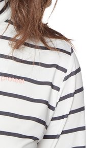 Biała bluzka z długim rękawem w poziome granatowe paski. Zawiera małe różowe logo "protest" na klatce piersiowej. Gładka tekstura, swobodny fason.