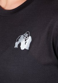 Crna majica kratkih rukava s reflektirajućim grafikom gorile. Tkanina je mrežasta, što omogućuje prozračnost i textured izgled.