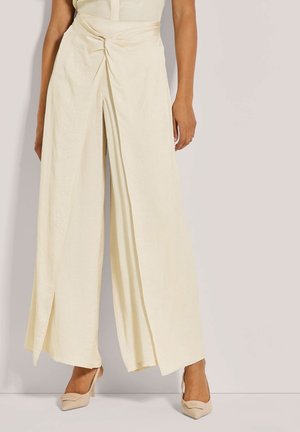 Crème kleurige wijde broek met een geknoopte voorkant, gemaakt van lichtgewicht stof. Soepel textuur en vloeiende silhouet. Zachte natuurlijke kleur.