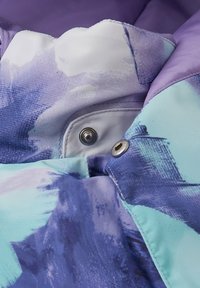 Interno di giacca multicolore con un mix di blu chiaro e scuro, motivi astratti viola, con bottoni a pressione e cuciture visibili.