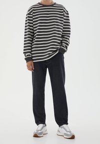Camisa de manga larga rayada en gris oscuro y blanco, con un escote redondo. Combinada con vaqueros negros de corte holgado y zapatillas deportivas grises.