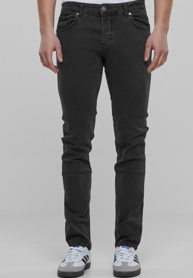 Črne denim kavbojke s slim fit krojem, petimi žepi in zapiranjem na gumb. Gladka tekstura in minimalne šivane podrobnosti, v kombinaciji s športnimi čevlji.